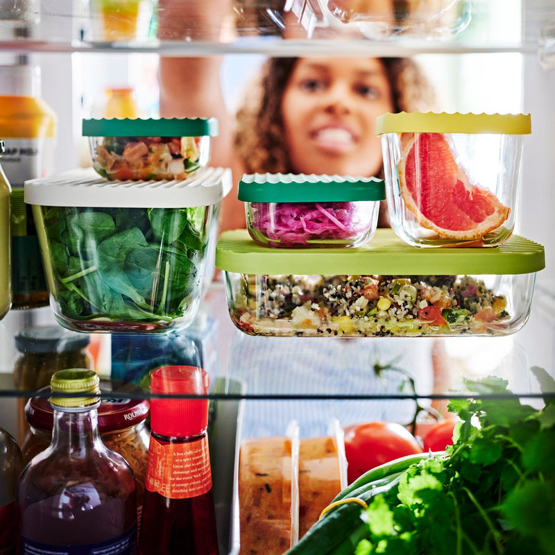A cut-through view of a refrigerator filled with HAVSTOBIS food containers. A person reaches in for one of the containers.