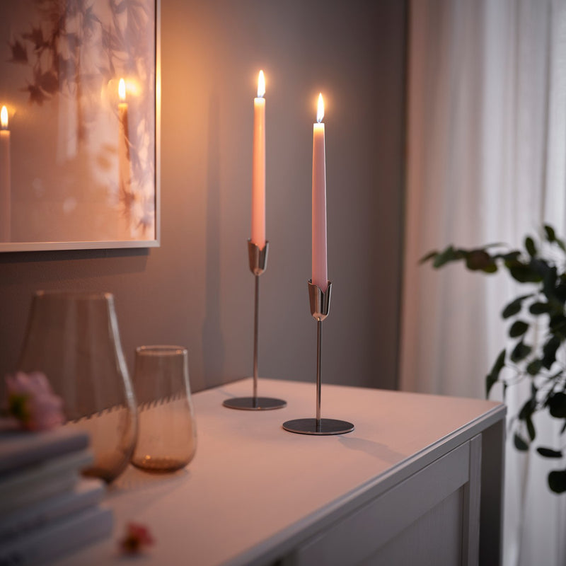 Un candeliere con due candele KLOKHET accese sopra un mobile e accanto a un quadro.
