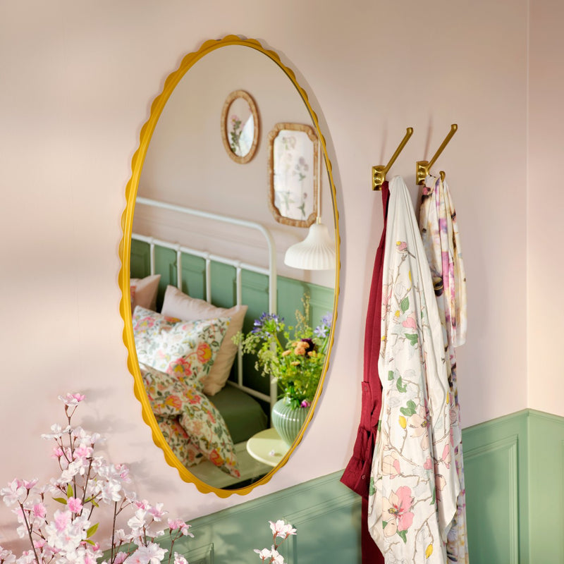 Uno specchio giallo scuro DAGGKAPRIFOL che riflette un'accogliente camera da letto con decorazioni floreali.